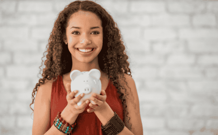 teenage girl smiling and holding a white piggy bank